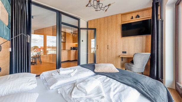 A modern hotel room with a large bed, a desk, a chair, a TV, and a sliding door leading to a balcony. - Apartamenty Sun & Snow Foka (Hel)