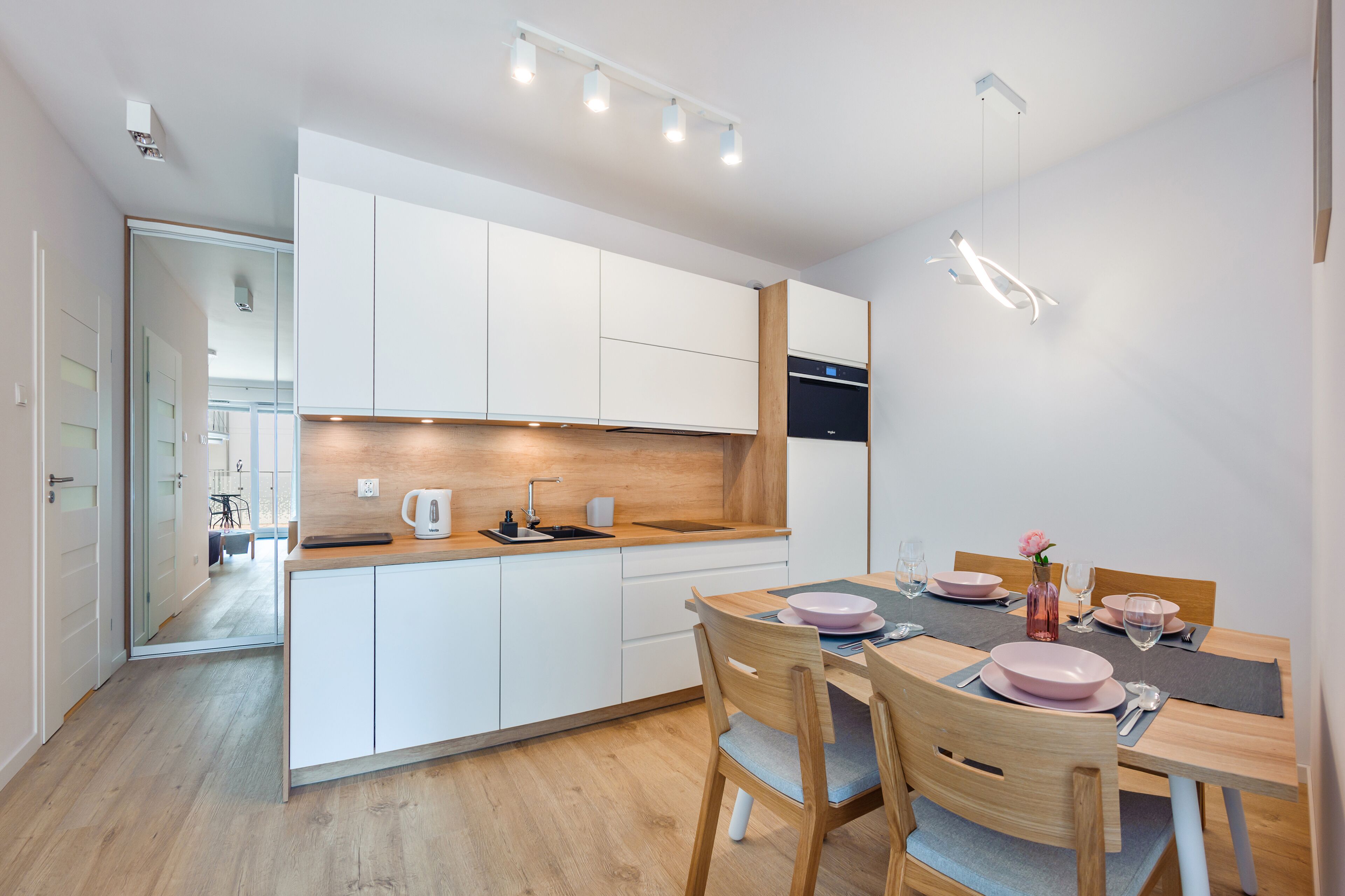 Una cocina moderna con armarios blancos, encimera de madera y un comedor con mesa preparada para cuatro personas.