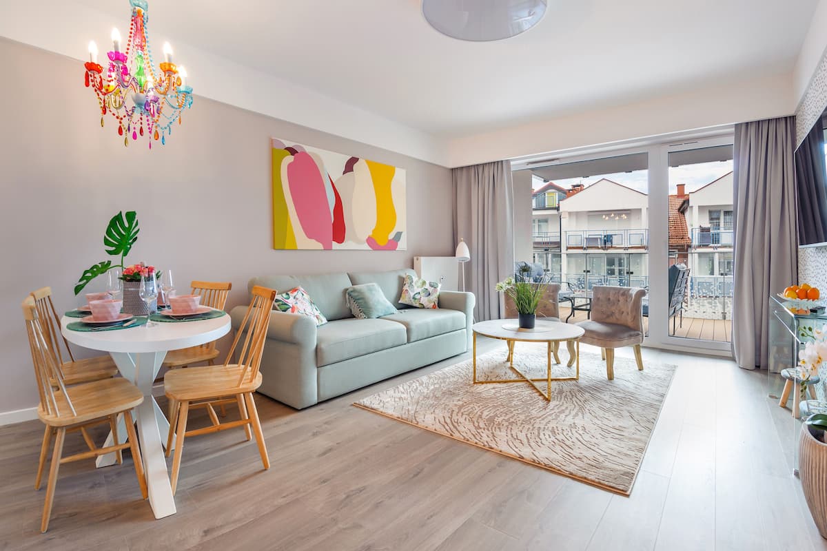 Uma sala de estar moderna com um sofá cinzento, cadeiras de madeira, uma mesa de centro redonda e um lustre.