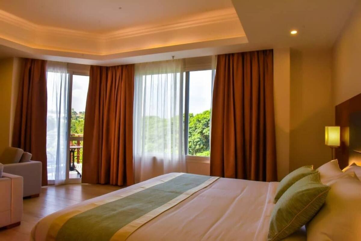 A hotel room with a large bed, a sofa, and a view of greenery outside.