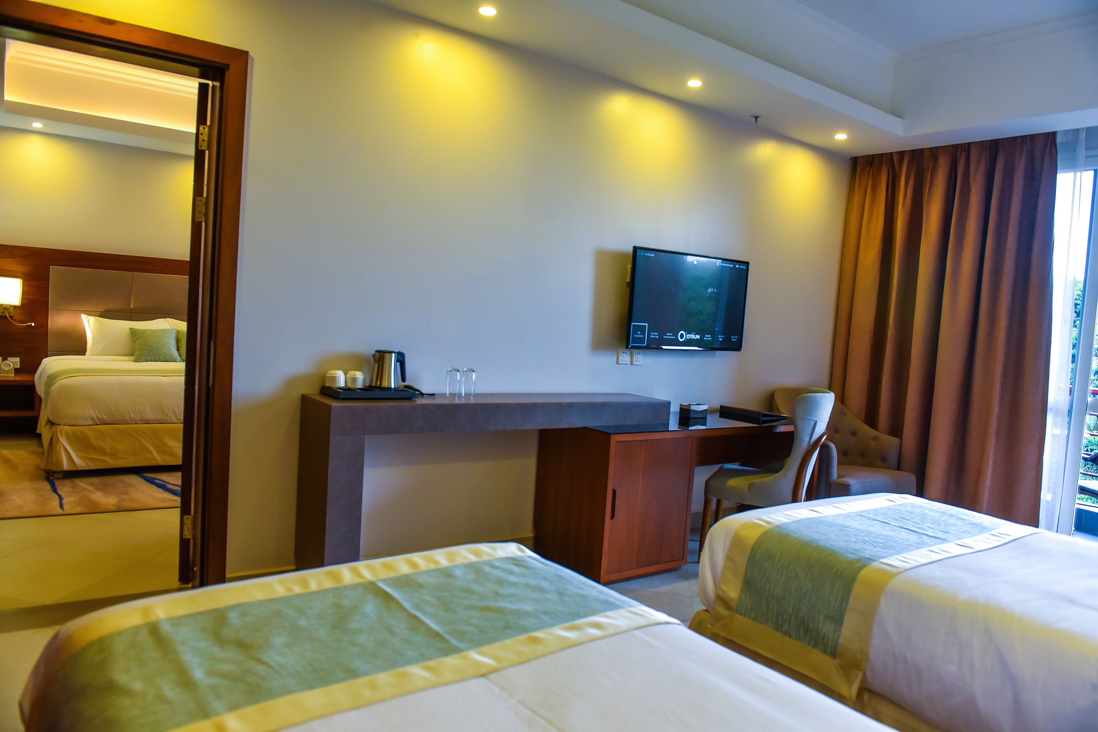 A hotel room with two beds, a desk, a television, and a view of the outdoors.