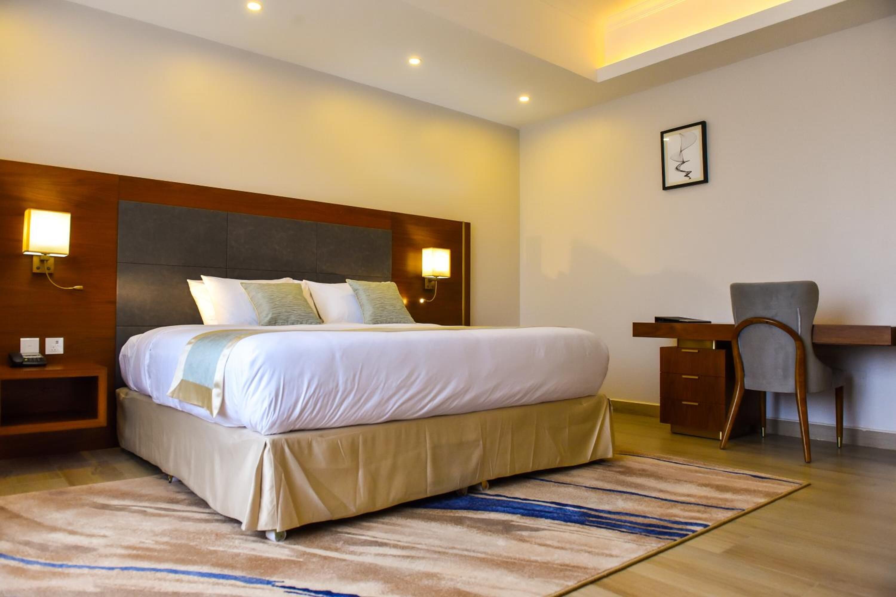 A hotel room with a large bed, bedside lamps, a desk, and a chair.