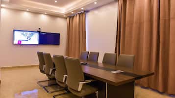 Una sala de conferencias con una mesa larga, seis sillas, un televisor de pantalla plana en la pared y cortinas marrones.