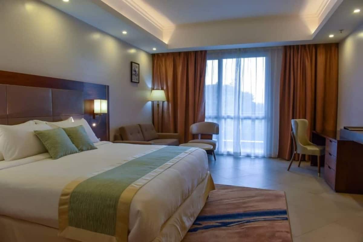 A hotel room with a large bed, a desk, a chair, a lamp, and a window with curtains.