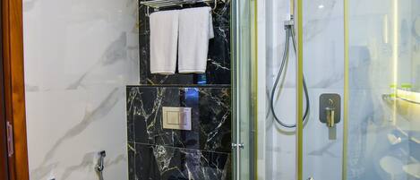 A modern bathroom with a glass-enclosed shower, marble walls, and a towel rack with two towels.