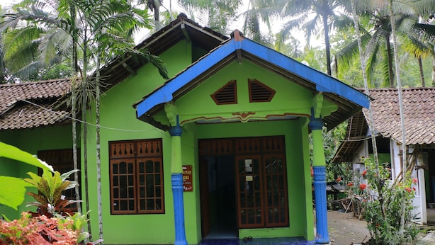 A green building with a tiled entrance, wooden doors, and a sign that reads "STAY SRI."