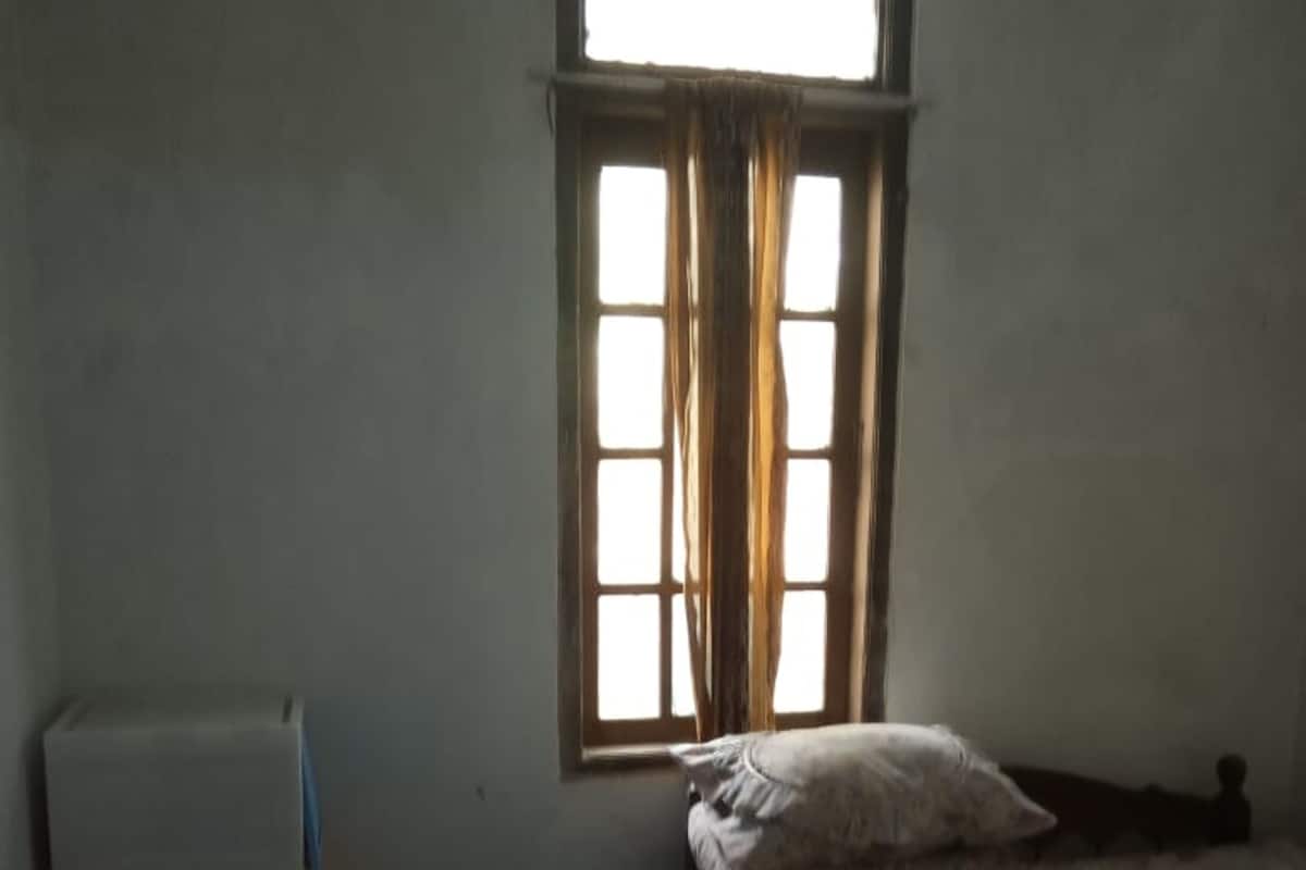 Una habitación pequeña y poco iluminada con una cama individual, una mesita y una ventana con cortinas.