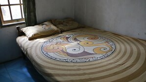 A single bed with a patterned bedspread and two pillows, a window with curtains, and a plain wall.