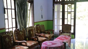 A room with wooden chairs and tables, large windows with curtains, and a green wall.