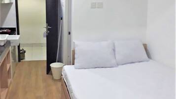 A bedroom with a bed, a nightstand, a trash bin, and a bathroom with a sink and mirror.