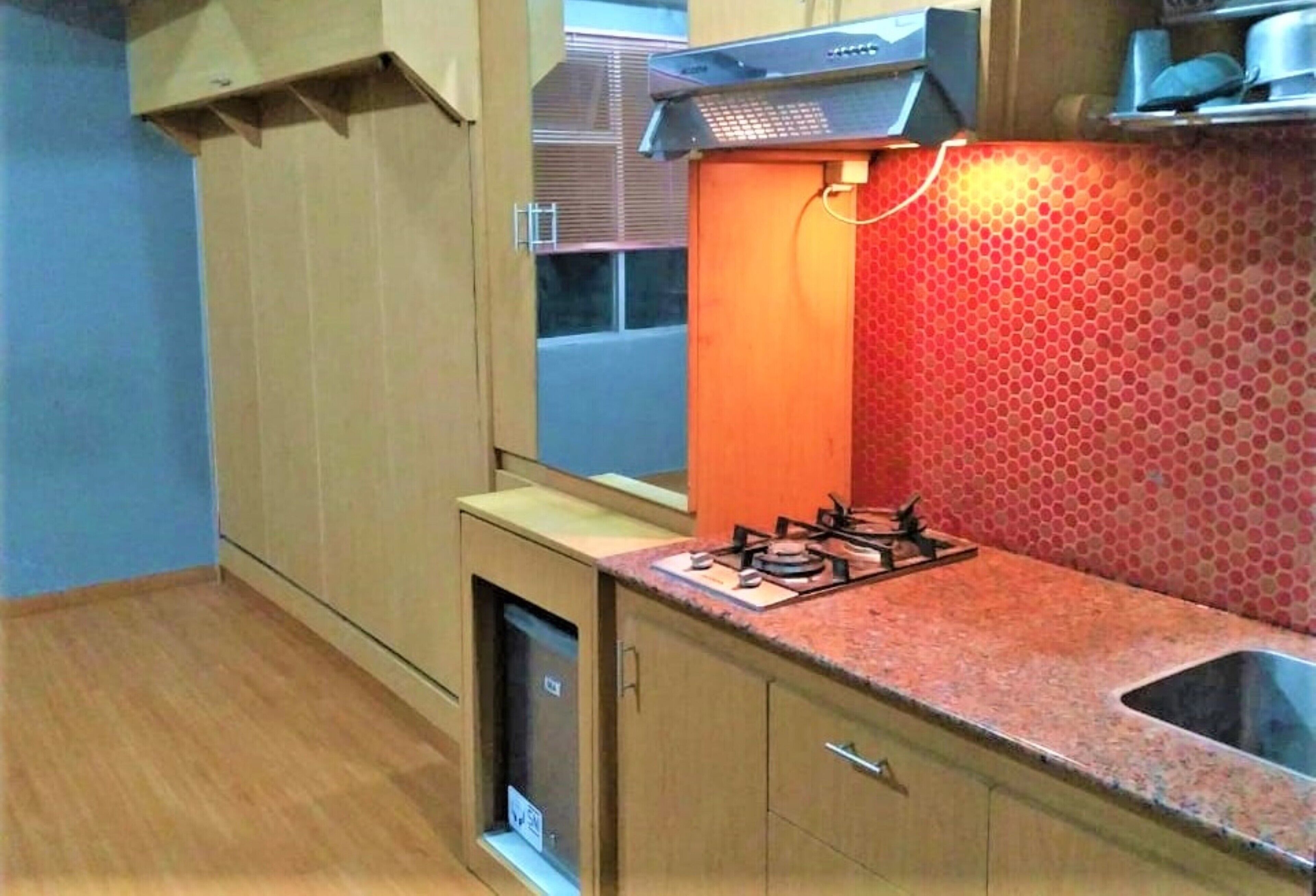 A compact kitchen with a gas stove, wooden cabinets, and a red tiled backsplash.