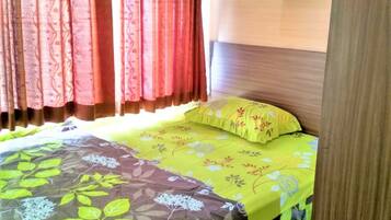 A bed with floral bedding, a wooden headboard, and red curtains.