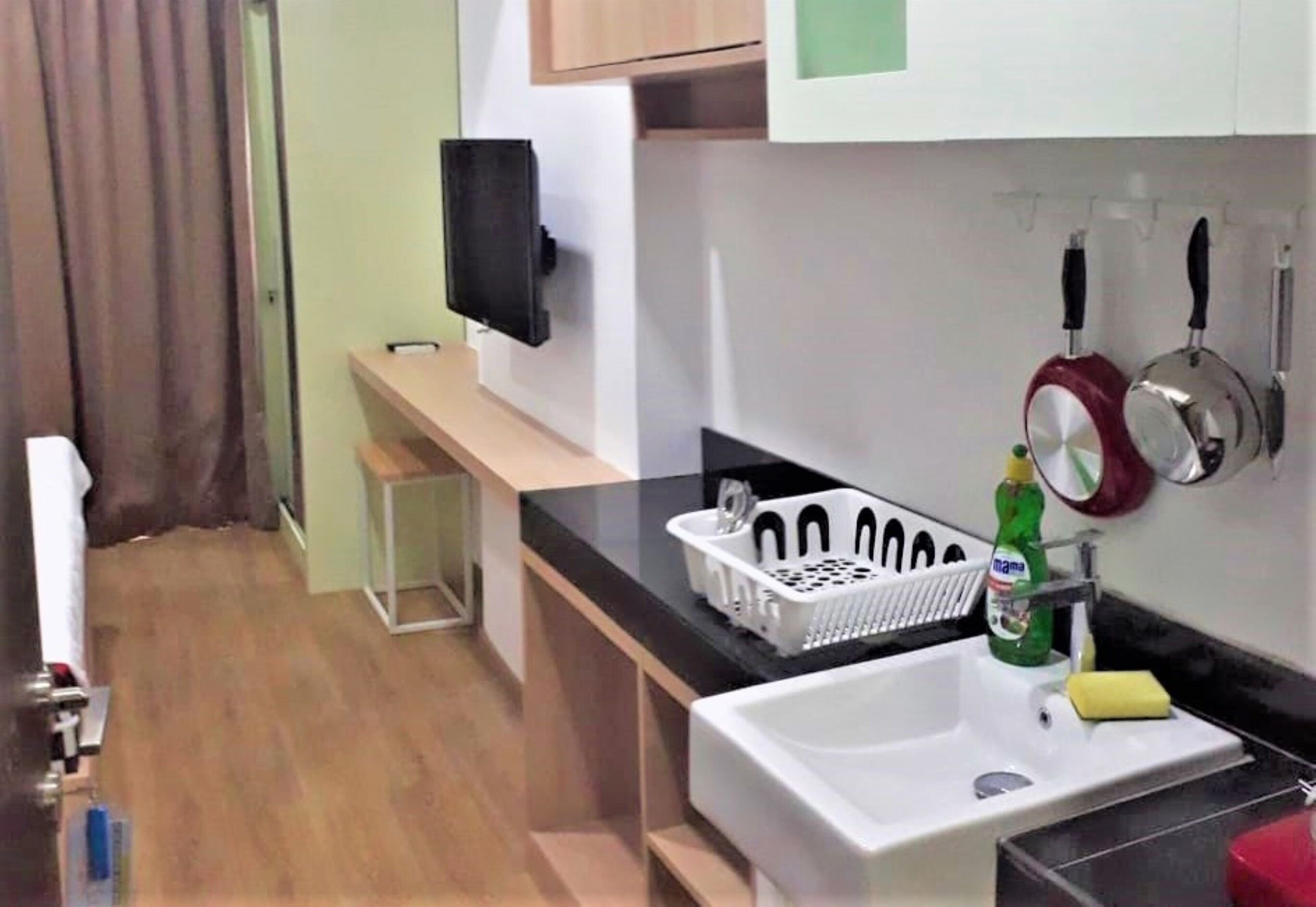 A compact kitchen with a sink, a small countertop, a television mounted on the wall, and a few kitchen utensils hanging above the sink.