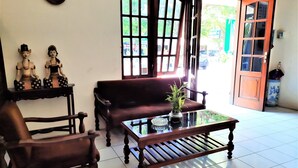 A room with a wooden sofa, a glass-top table with a vase, and two wooden chairs. - Hotel Perdana (Klaten)