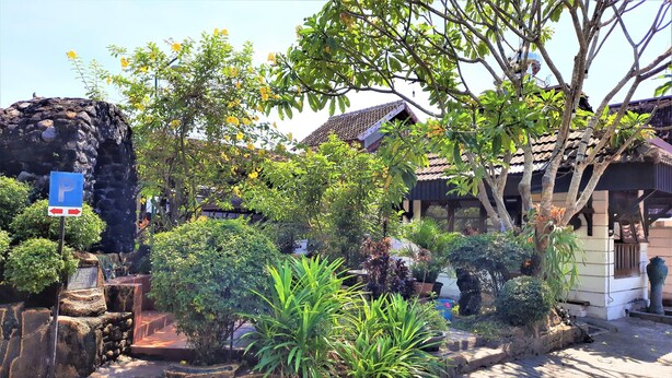 A traditional building with a tiled roof, surrounded by lush greenery and a stone structure. - Hotel Perdana (Klaten)