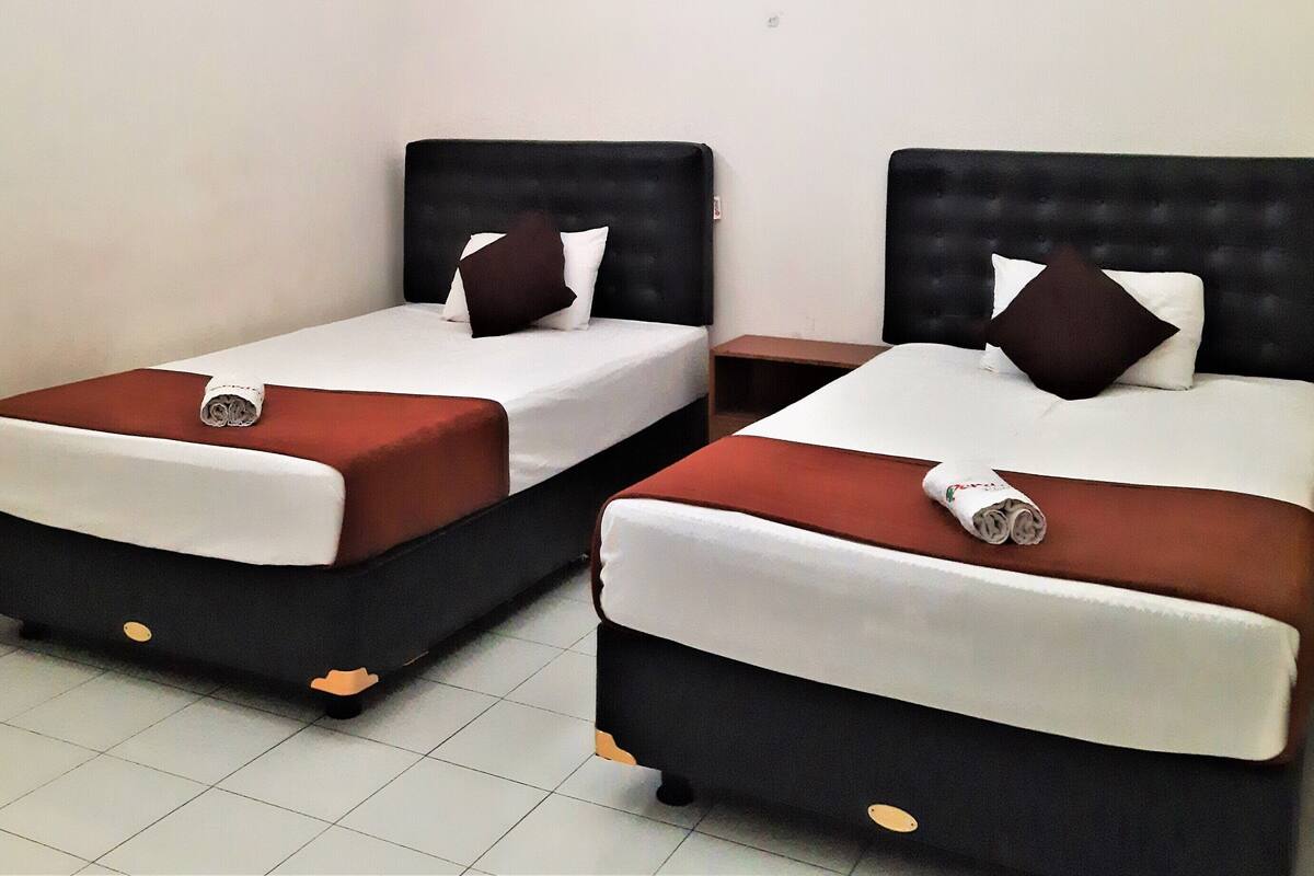 Two single beds with black headboards and white bedding, each with a brown pillow and a rolled towel on the footboard.