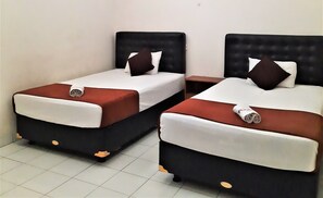 Two single beds with black headboards and white bedding, each with a brown pillow and a rolled towel on the footboard. - Hotel Perdana (Klaten)