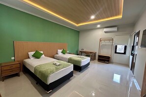A hotel room with two beds, a desk, a mirror, and a small seating area. - Hotel Perdana (Klaten)