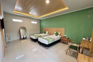 A hotel room with two beds, a desk, a chair, a mirror, and a green accent wall. - Hotel Perdana (Klaten)
