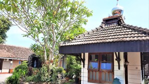A traditional building with a tiled roof, a statue in front, and a large tree. - Hotel Perdana (Klaten)