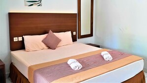 A neatly made bed with a wooden headboard, a pink pillow, and a checkered blanket. - Hotel Perdana (Klaten)