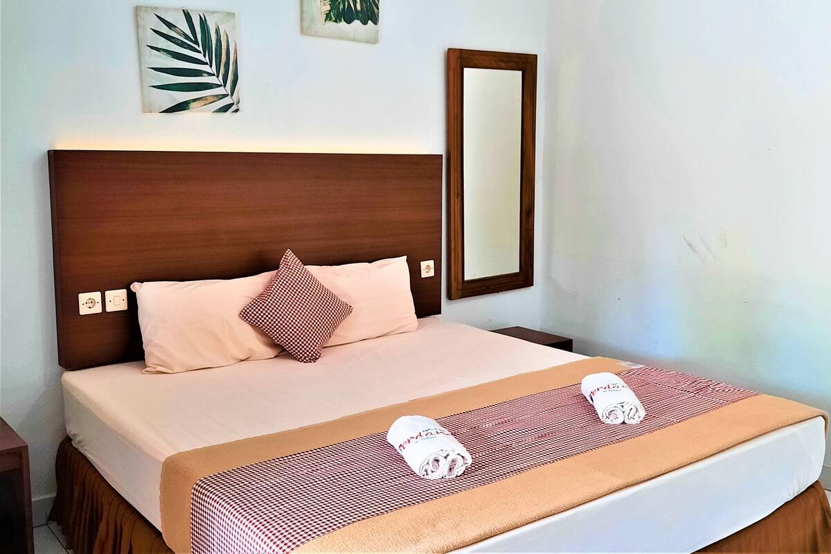 A neatly made bed with a wooden headboard, a pink pillow, and a checkered blanket.