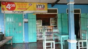 Pequeña tienda abierta con puertas turquesas y un interior azul. Hay estantes llenos de diversos productos y un cartel que anuncia 4GB de datos móviles.