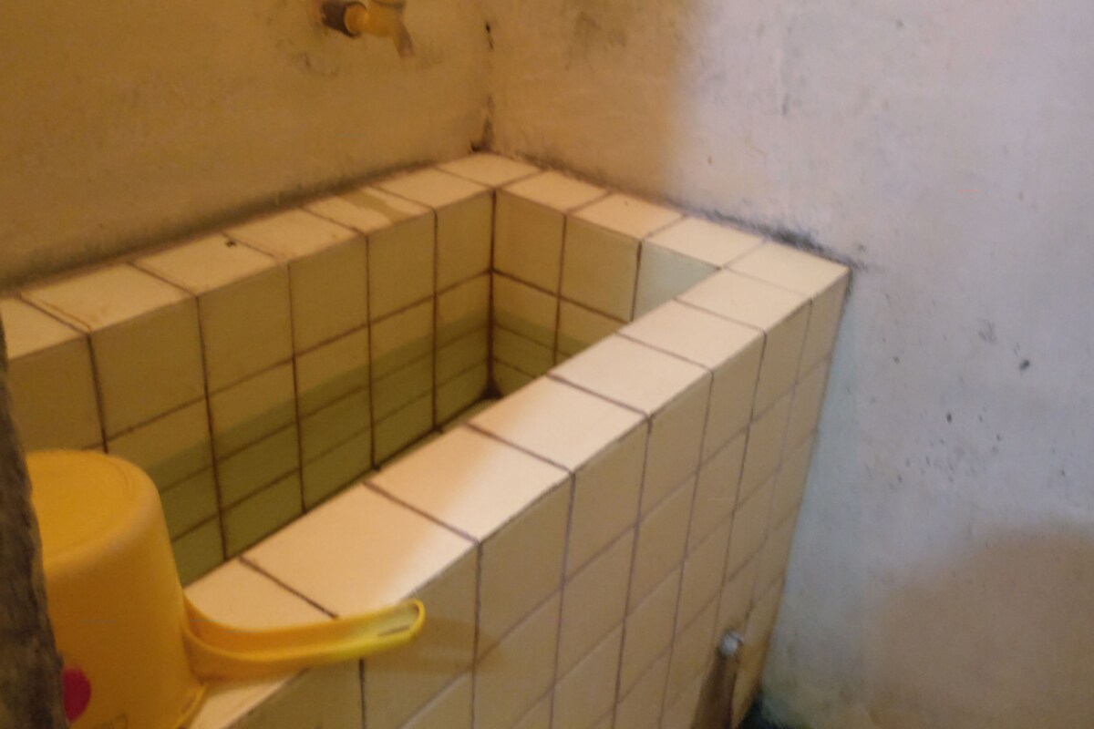A bathroom with a tiled shower area, a yellow toilet, and a visible pipe on the wall.