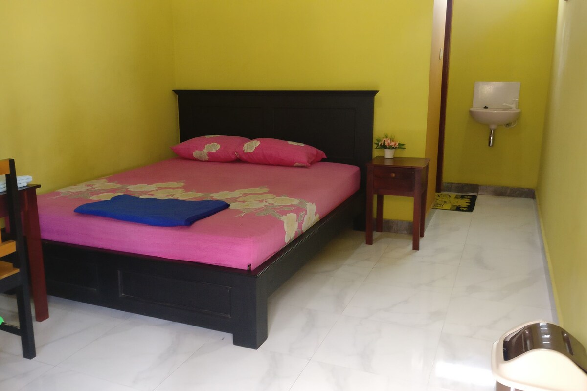 A room with a bed, a chair, a nightstand, and a wall-mounted light fixture.