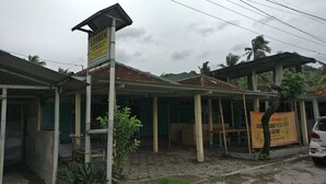 Un edificio con un cartel, un espacio de estar al aire libre cubierto y un coche estacionado.