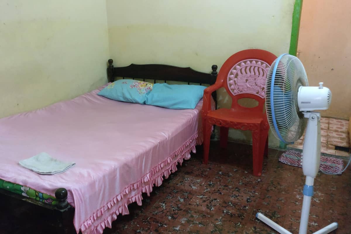 A small room with a single bed, a chair, and a standing fan.