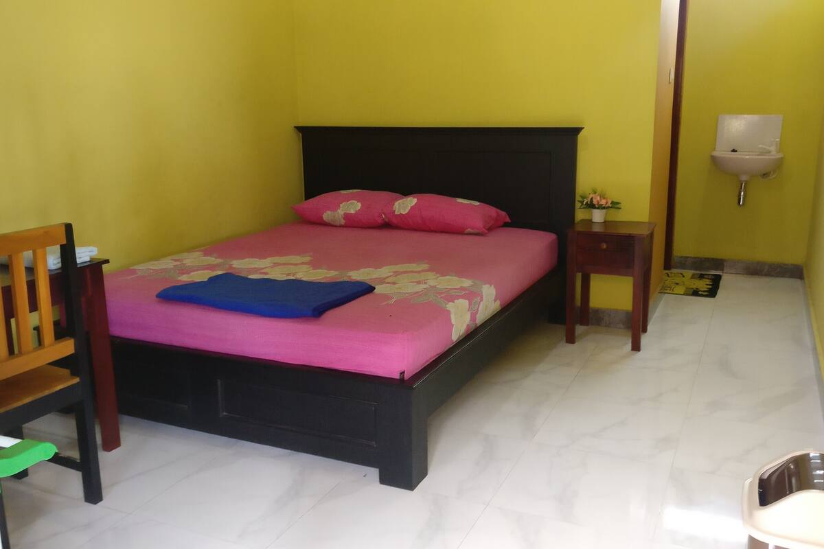 A room with a bed, a chair, a nightstand, and a wall-mounted light fixture.