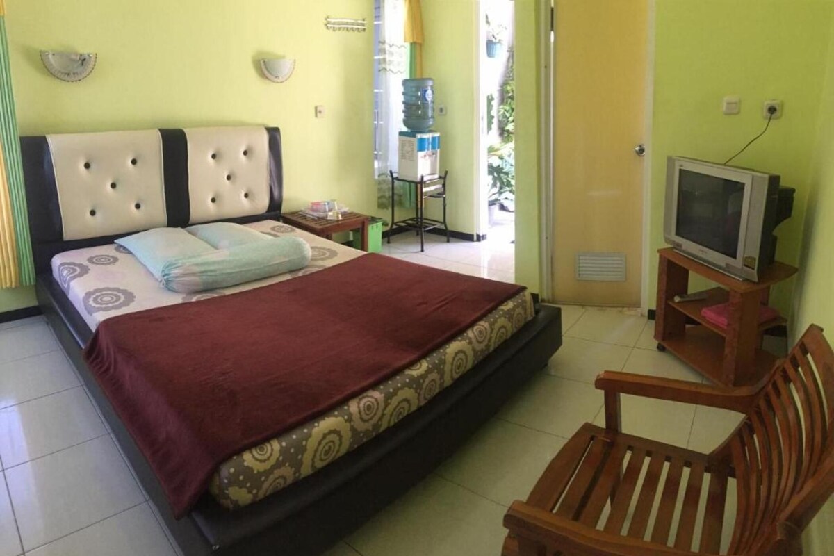 A bedroom with a bed, a television on a stand, a chair, and a water dispenser.