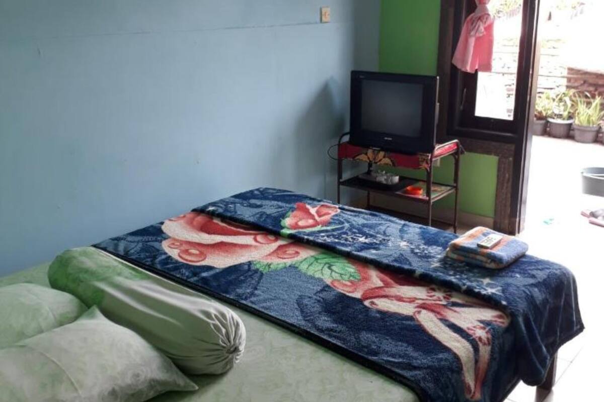 Una habitación pequeña con una cama, un televisor sobre un soporte y una ventana con cortina.