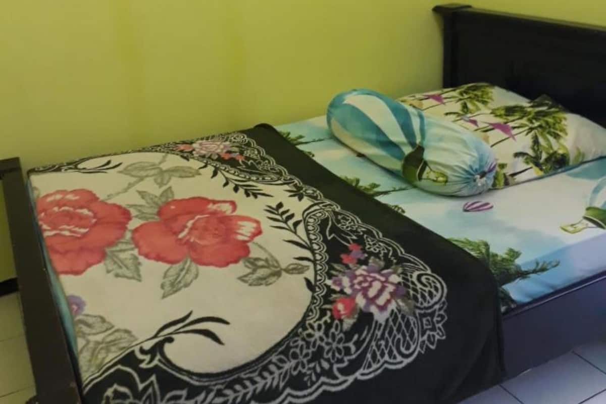 Una cama con ropa de cama floral y cabecera negra en una habitación con paredes amarillas.