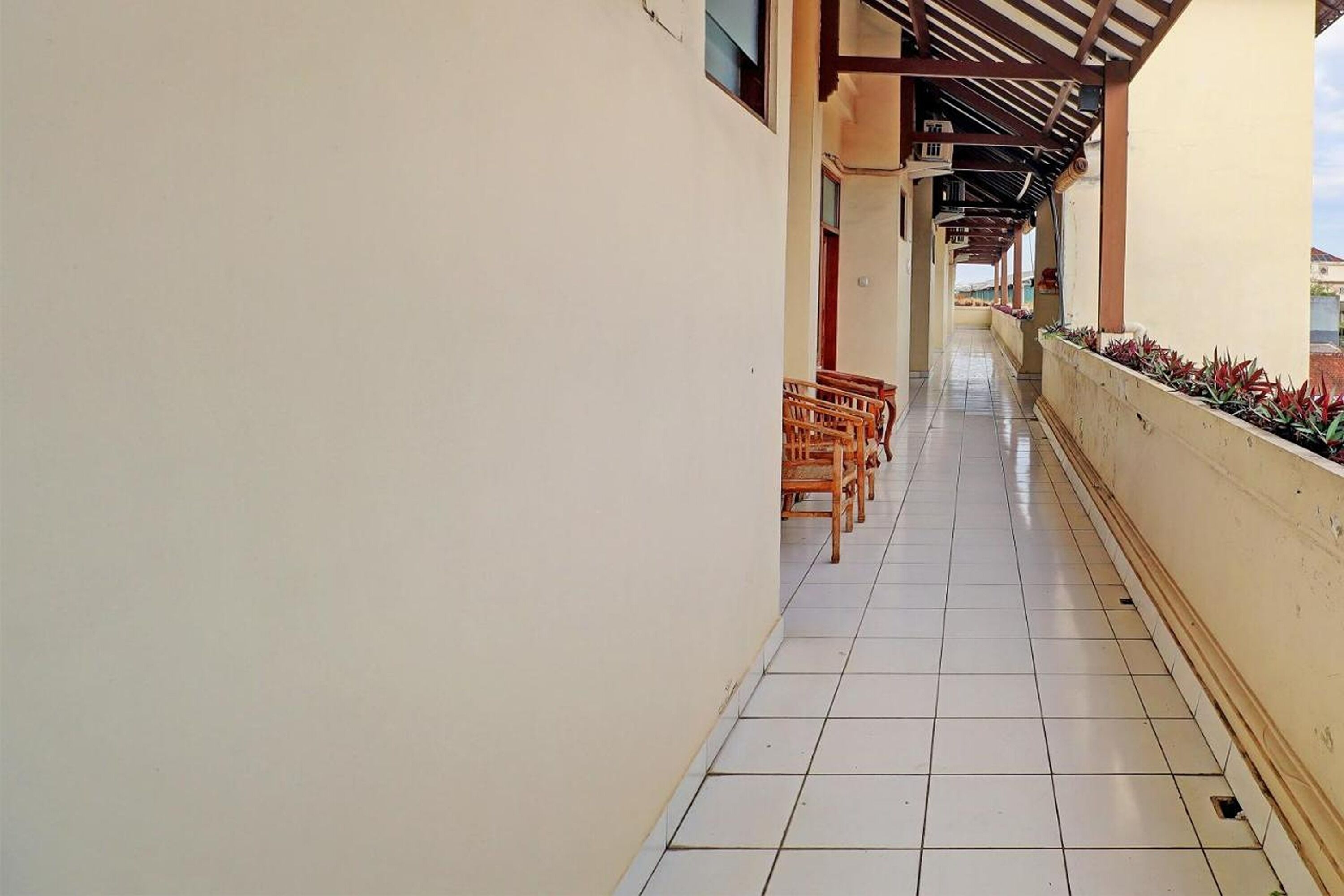 A corridor with tiled flooring, wooden chairs, and a tiled wall.