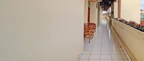 A corridor with tiled flooring, wooden chairs, and a tiled wall.