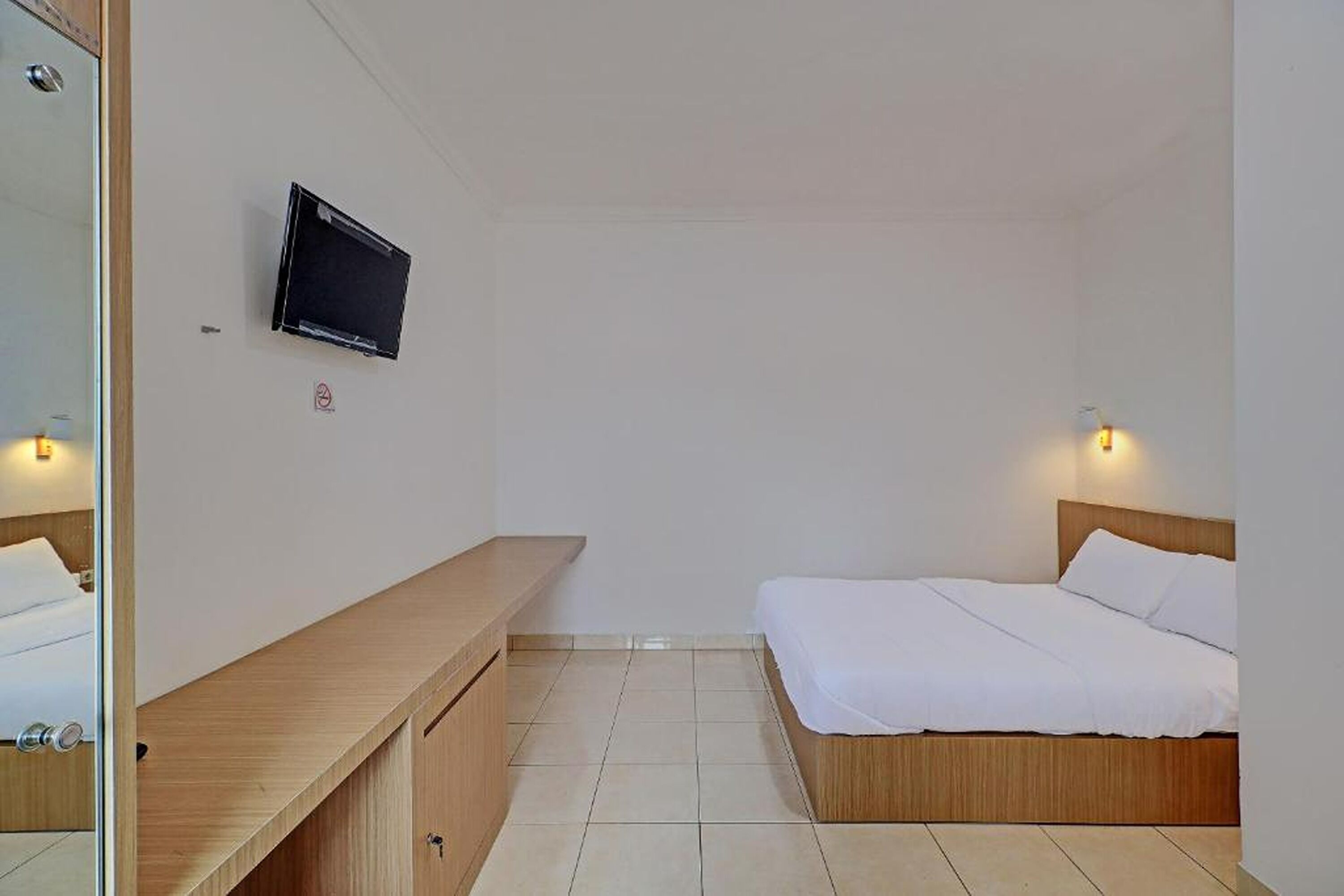 Een hotelkamer met een bed, nachtkastje, een aan de muur bevestigde televisie en een klein plankje.