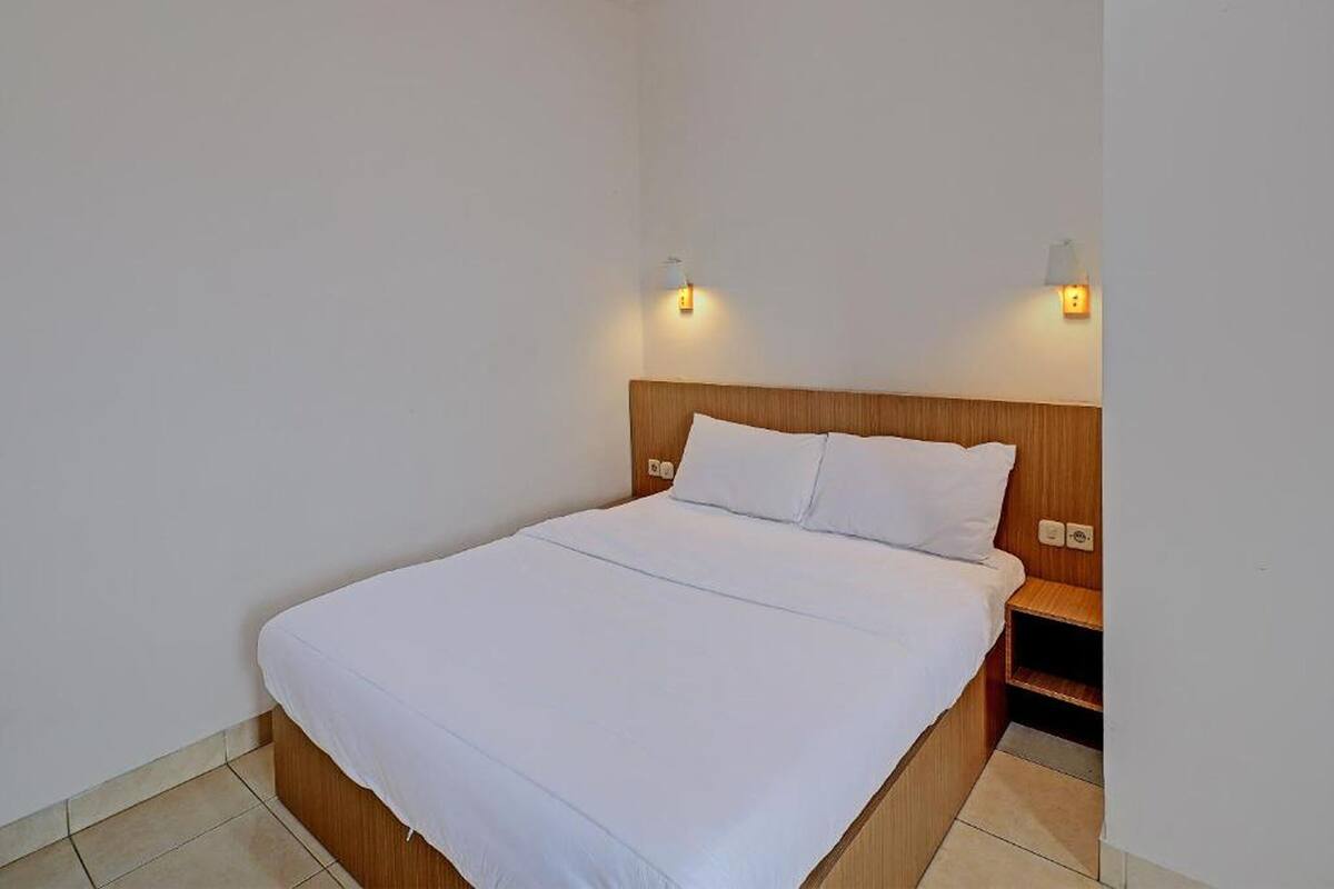 A single bed with a wooden headboard, white bedding, and two wall-mounted light fixtures.