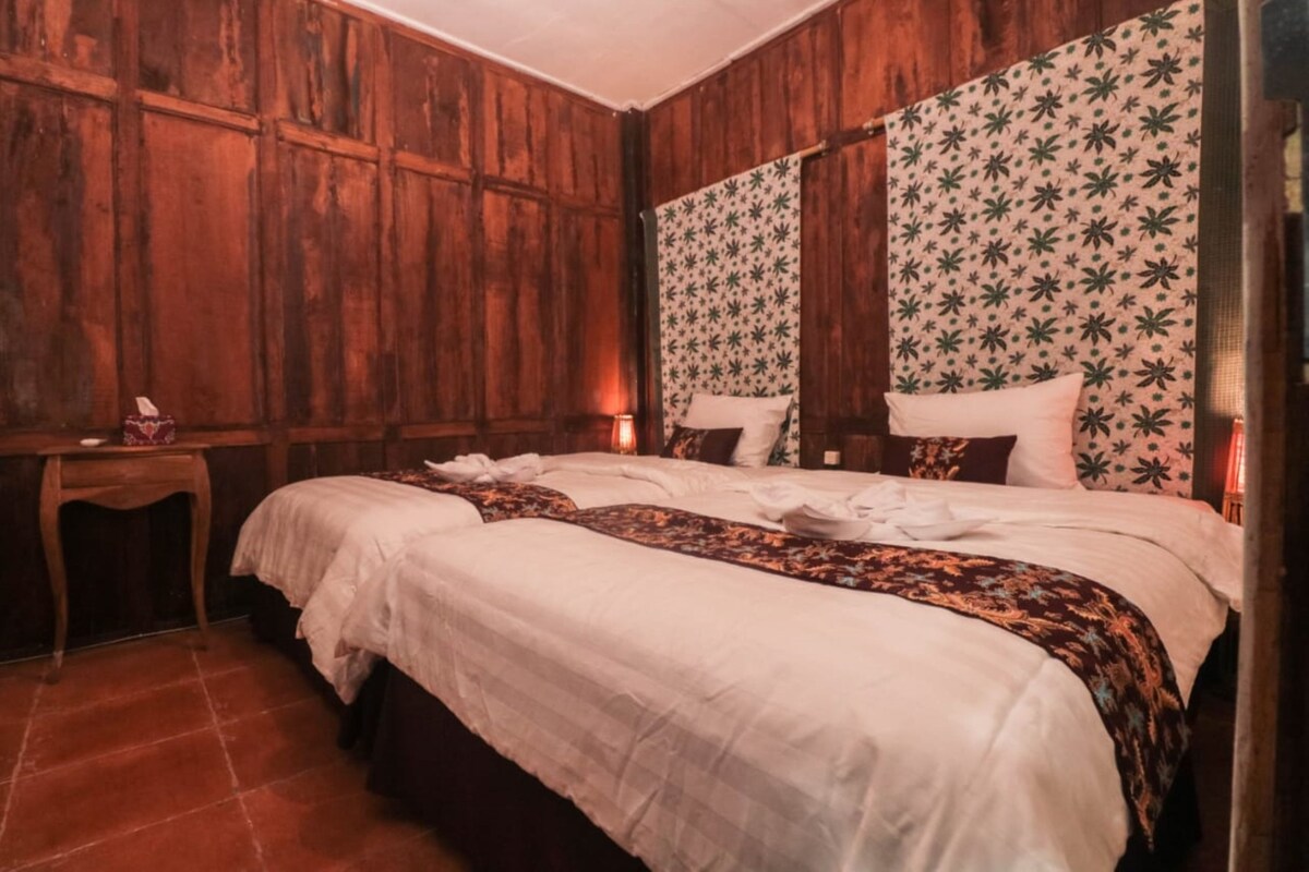 A room with wooden paneling, a bed with white linens, a patterned wall, and a small table with a lamp.