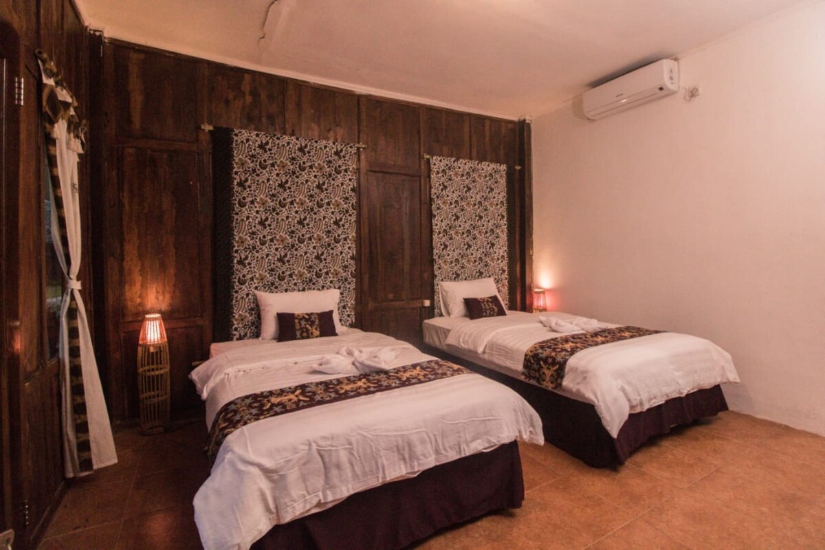 Een kamer met twee bedden, houten wanden, kamer met gordijnen met een patroon en een wandairconditioner.