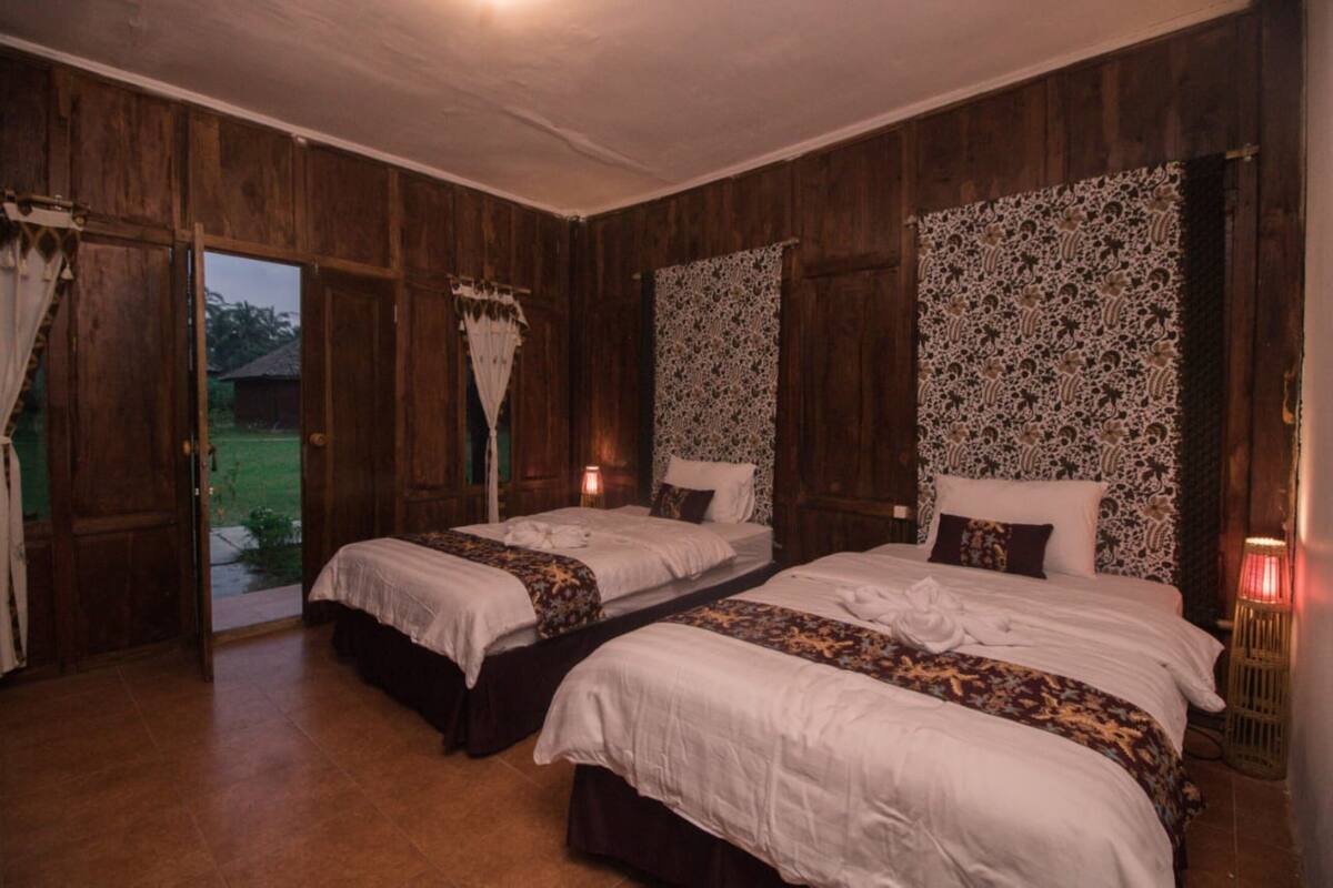 Ein Zimmer mit zwei Betten, Holzwänden und Blick ins Freie.