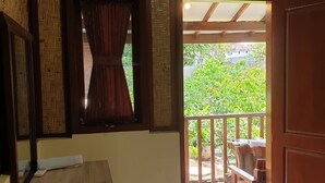 Een kamer met een houten bureau, een raam met gordijn en uitzicht op een balkon met tuinmeubilair.