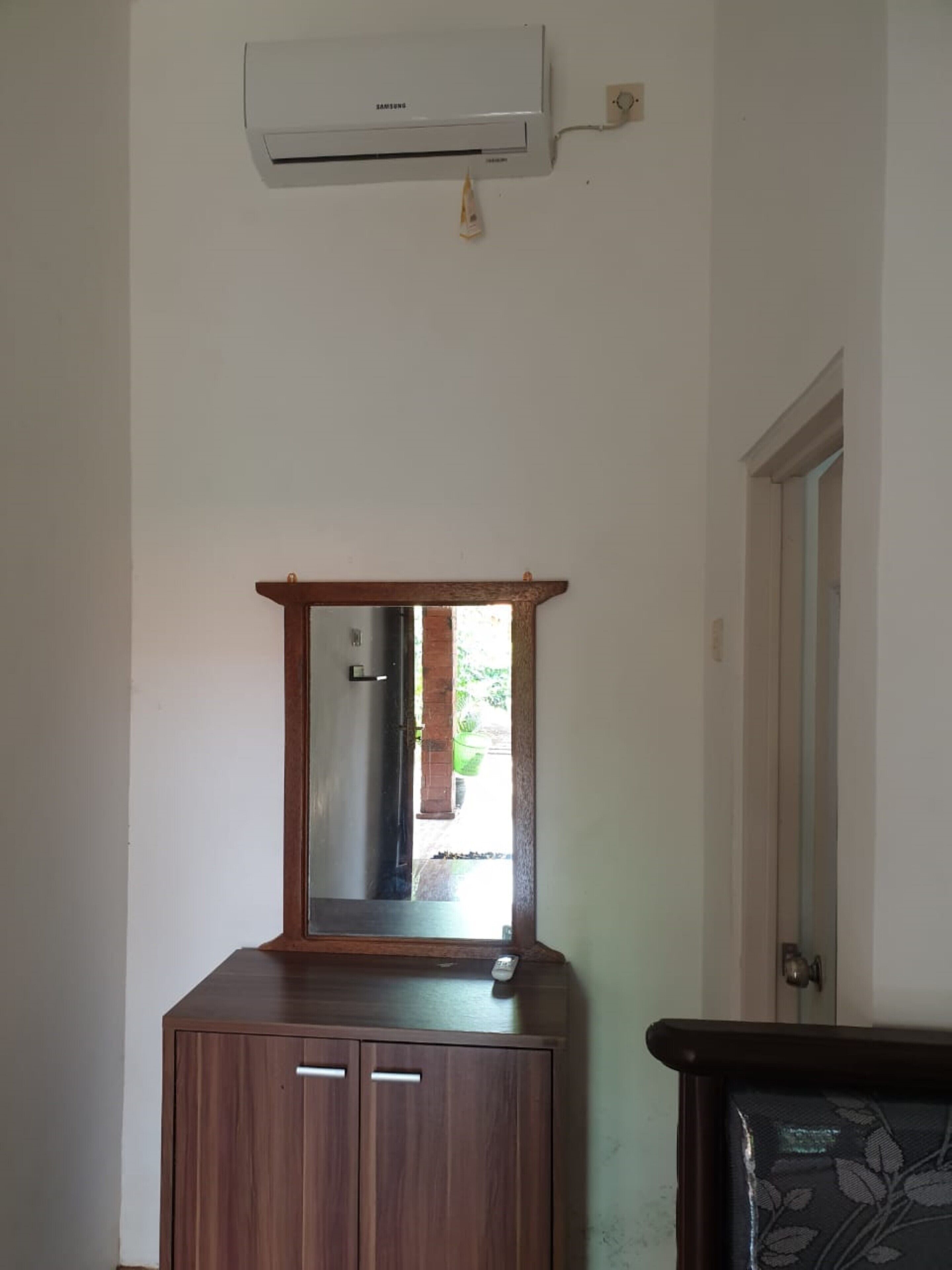 A room with a wooden cabinet, a mirror, and an air conditioning unit mounted on the wall.