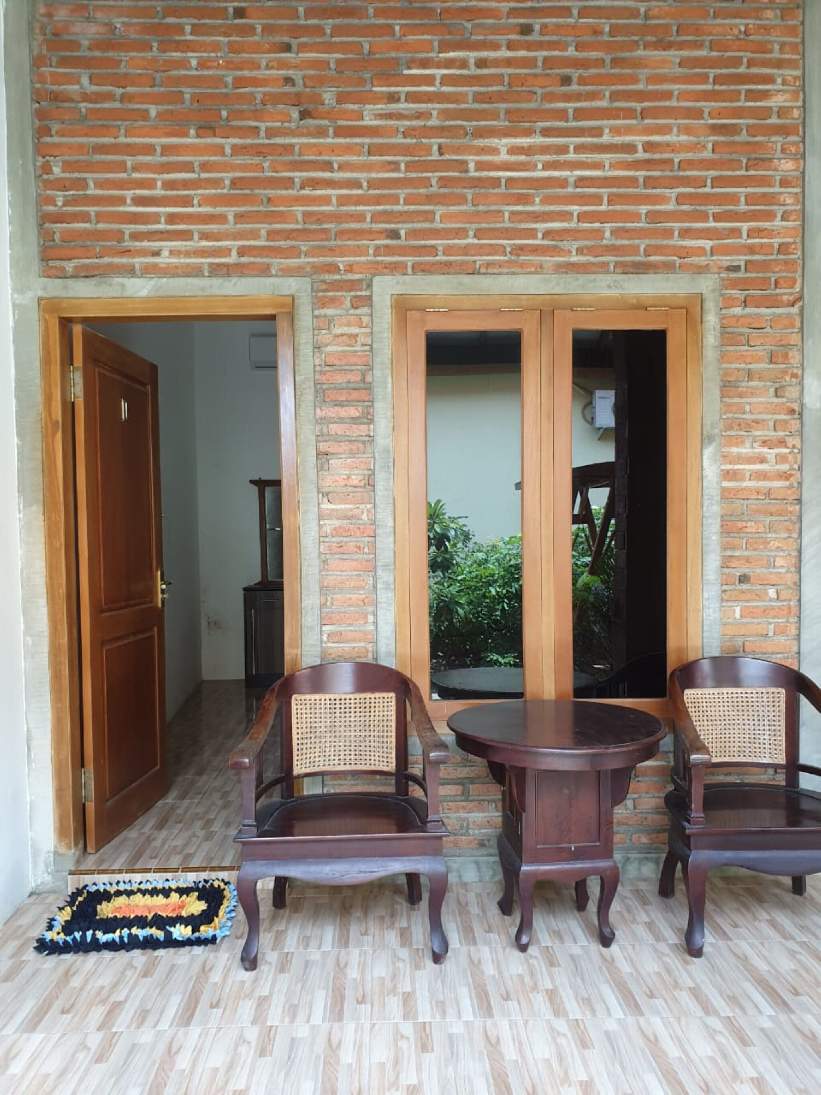 Um quarto com parede de tijolos, porta de madeira e duas cadeiras de madeira com assentos trançados.