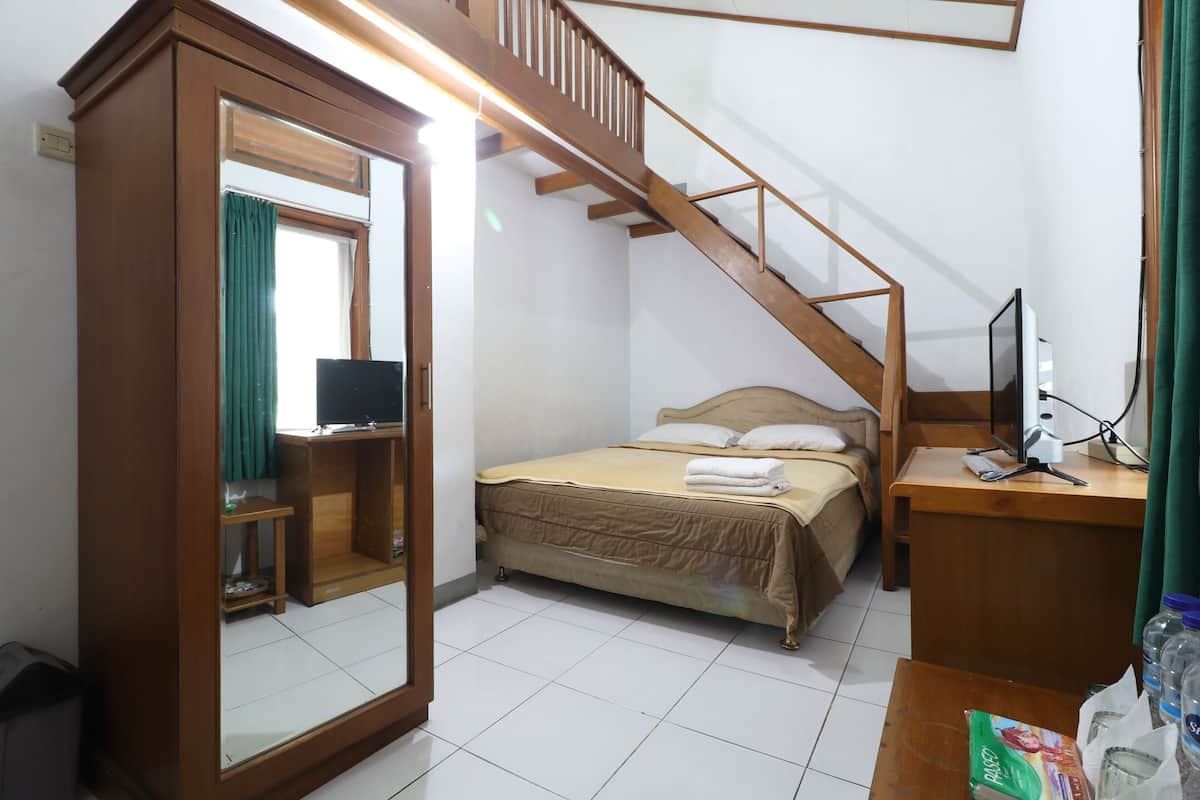A bedroom with a bed, a wooden desk, a mirror, a staircase, and a television.