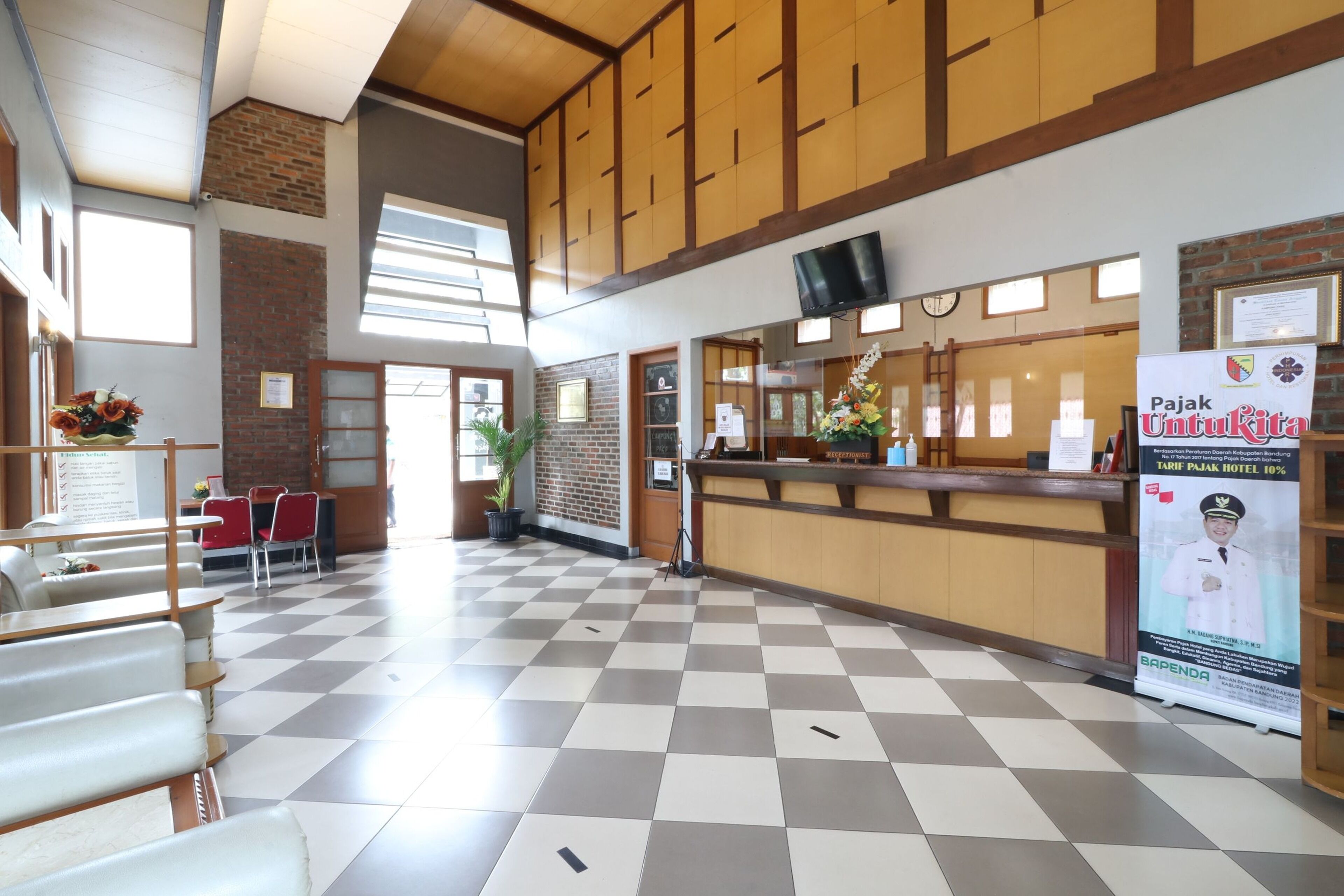 Un hall d’hôtel avec un sol à carreaux, un comptoir d’accueil en bois et une grande affiche publicitaire pour l’hôtel.