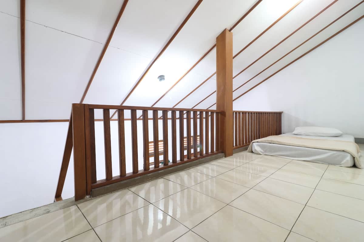 A room with a sloped ceiling, a bed with white bedding, and a wooden railing.