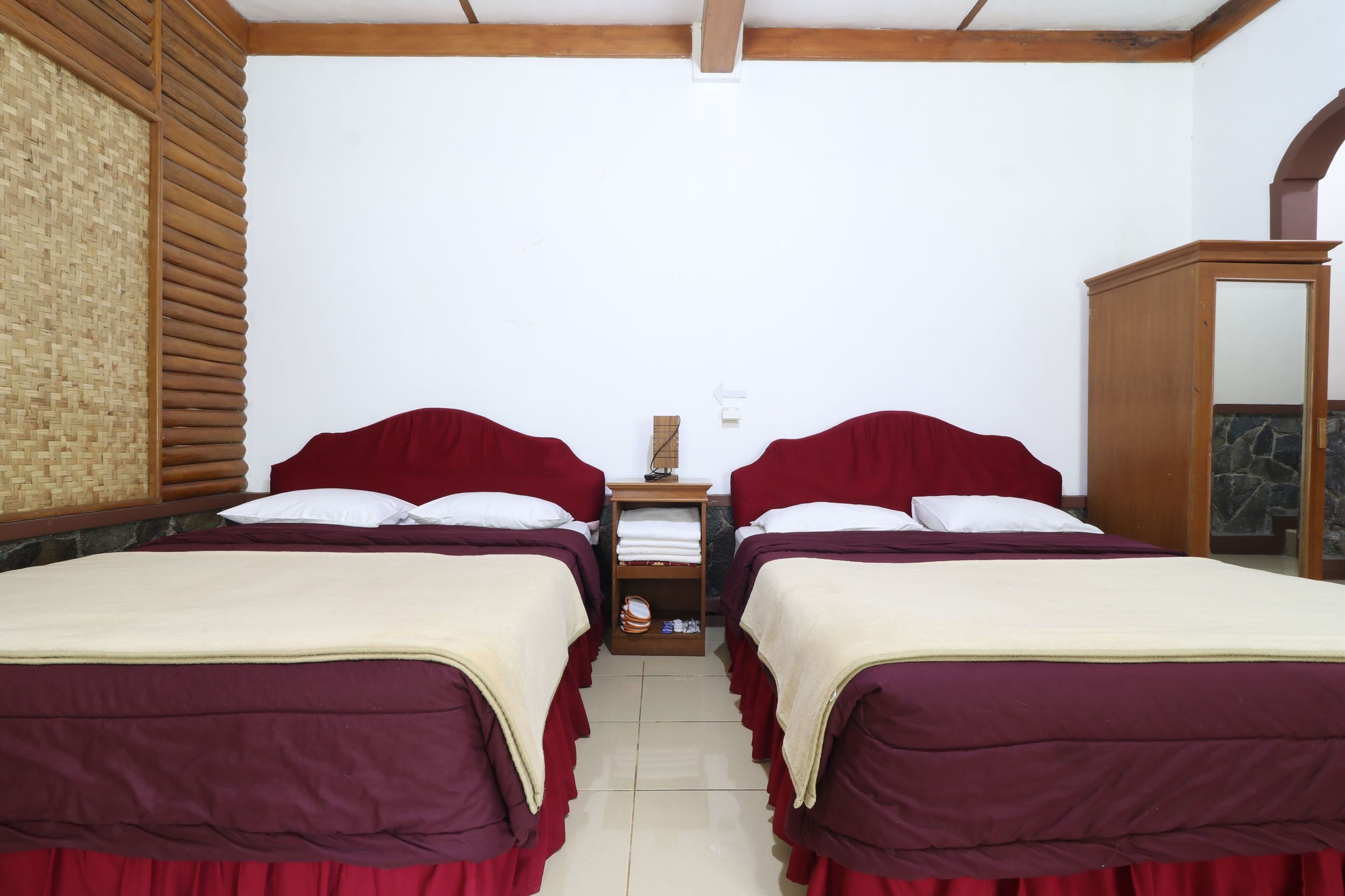 A room with two beds, a wooden wardrobe, and a small table with a lamp.
