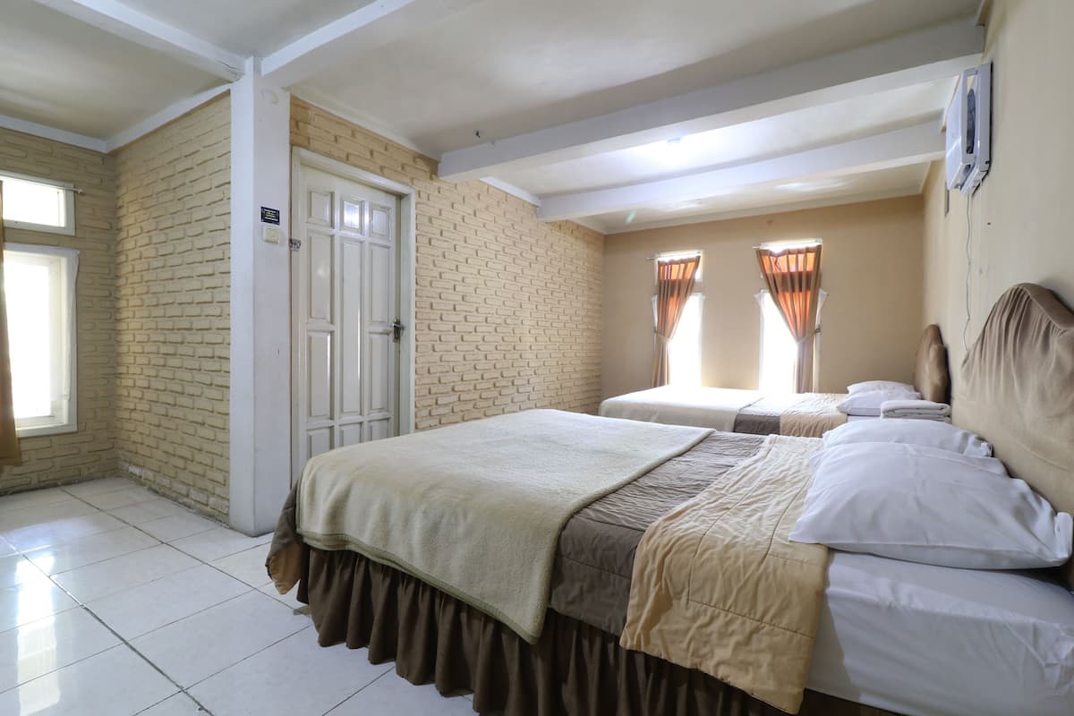A hotel room with two beds, a brick wall, a door, and a window with curtains.